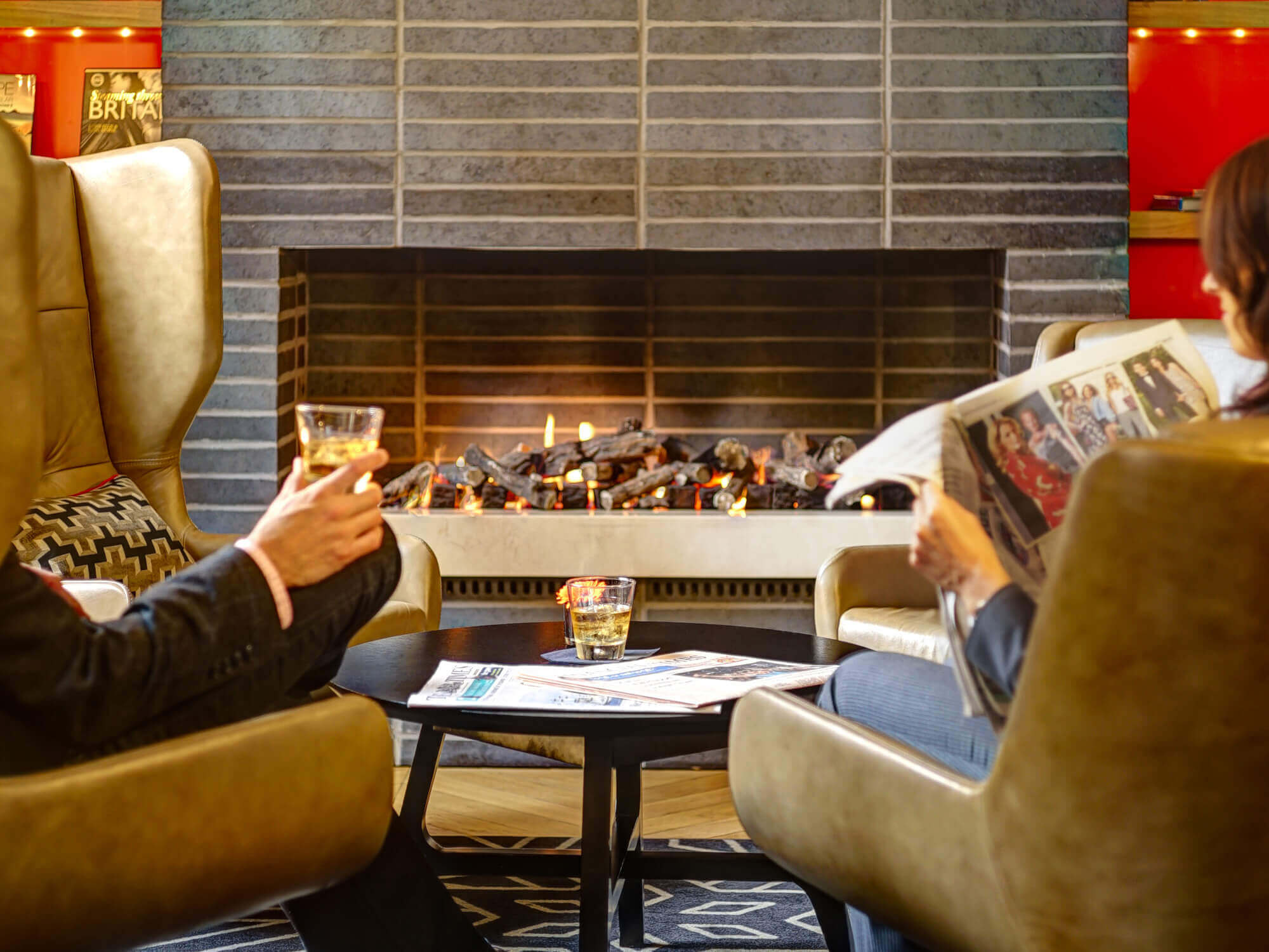 Two people drinking and reading the newspaper by the fireplace Two people drinking and reading the newspaper by the fireplace